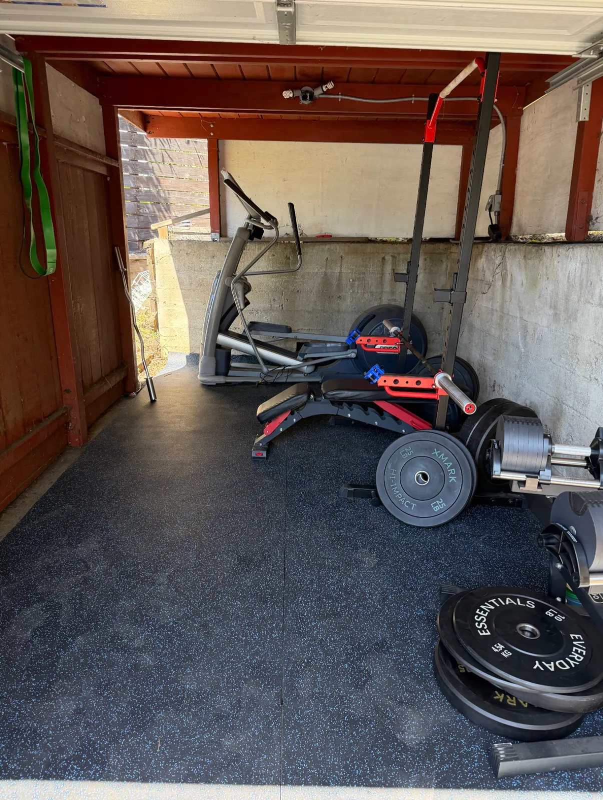 Home gym with a squat rack, bench, bumper plates and an elliptical on rubber flooring