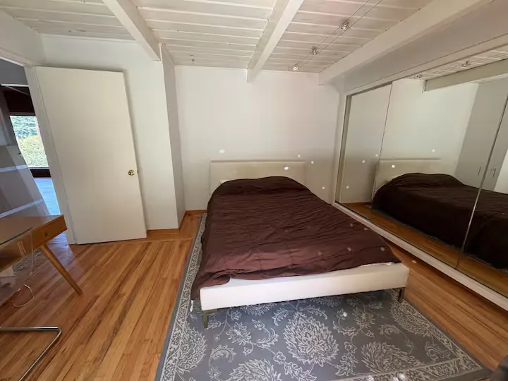 The bedroom from the doorway, with hardwood floors and a mirrored closet wall