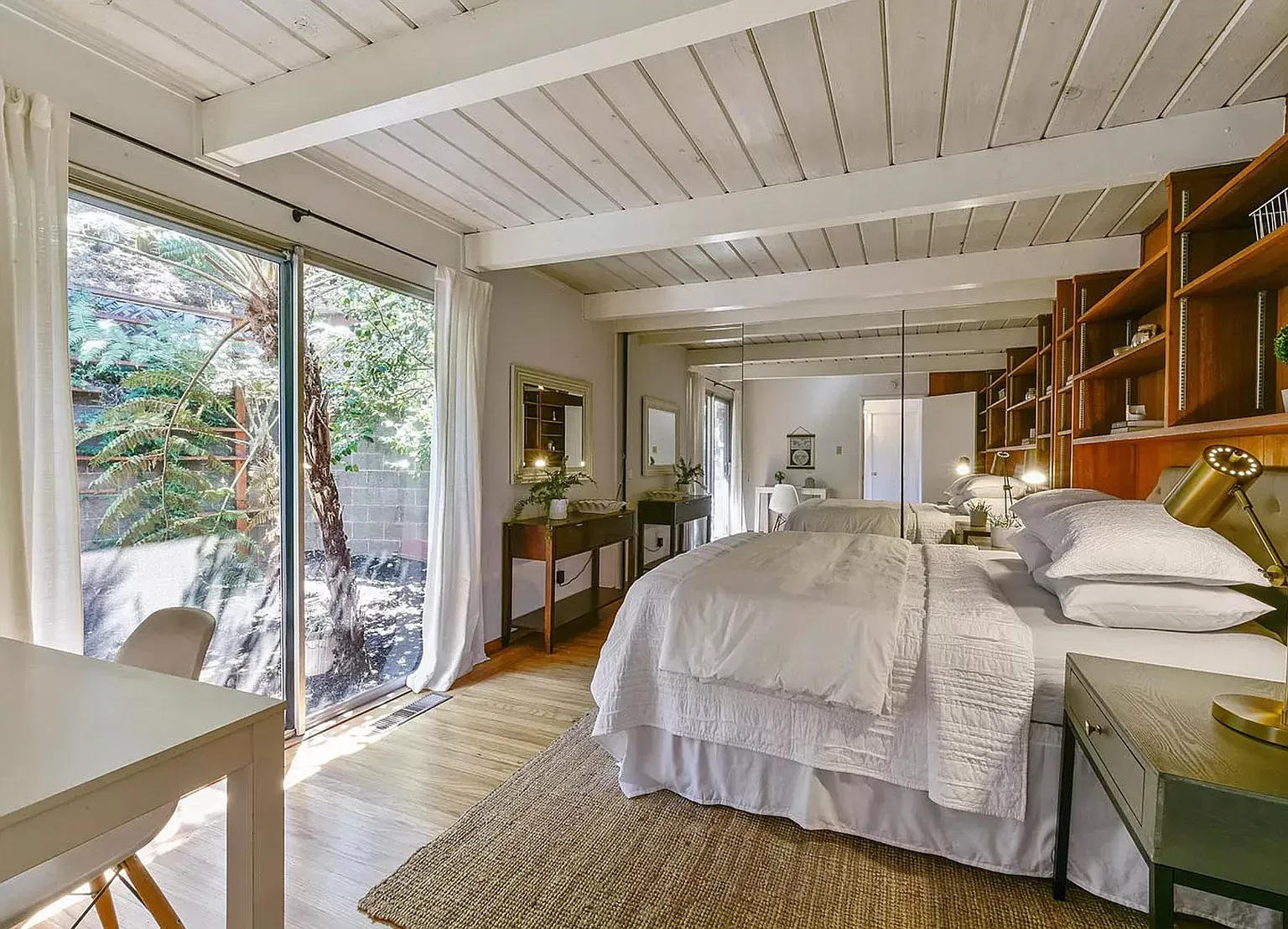 The second bedroom styled with a white bed, desk and a glass slider onto a fern garden