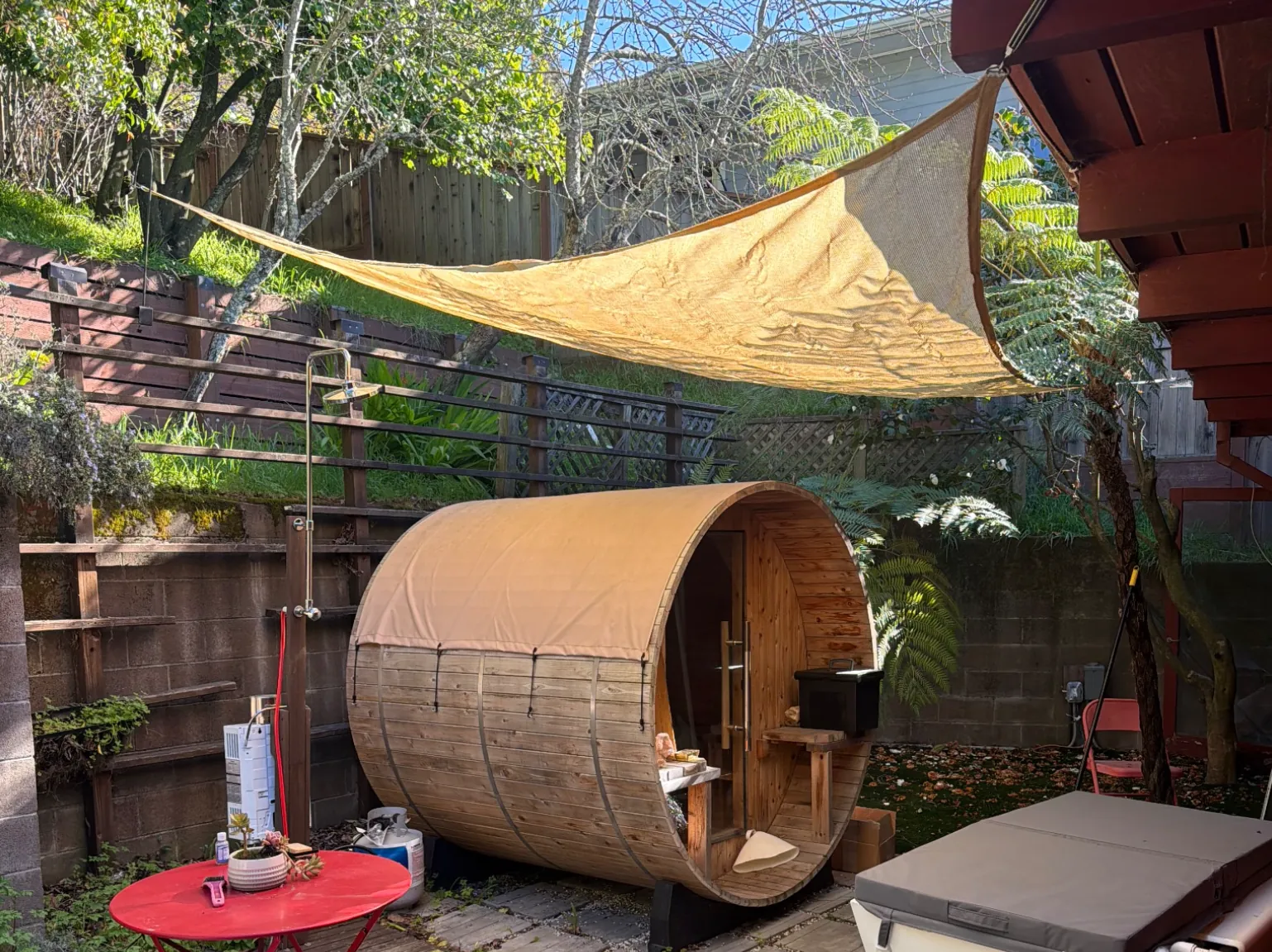 The outdoor shower beside the cedar barrel sauna on the back patio, under a sail shade